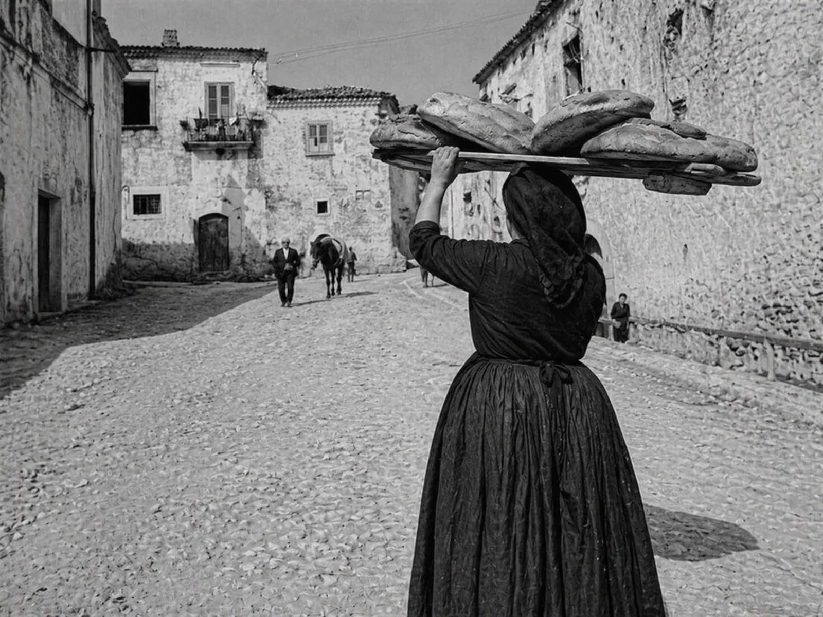 Donna che trasporta il pane di Matera su una tavola nei Sassi di Matera, in una scena storica in bianco e nero.