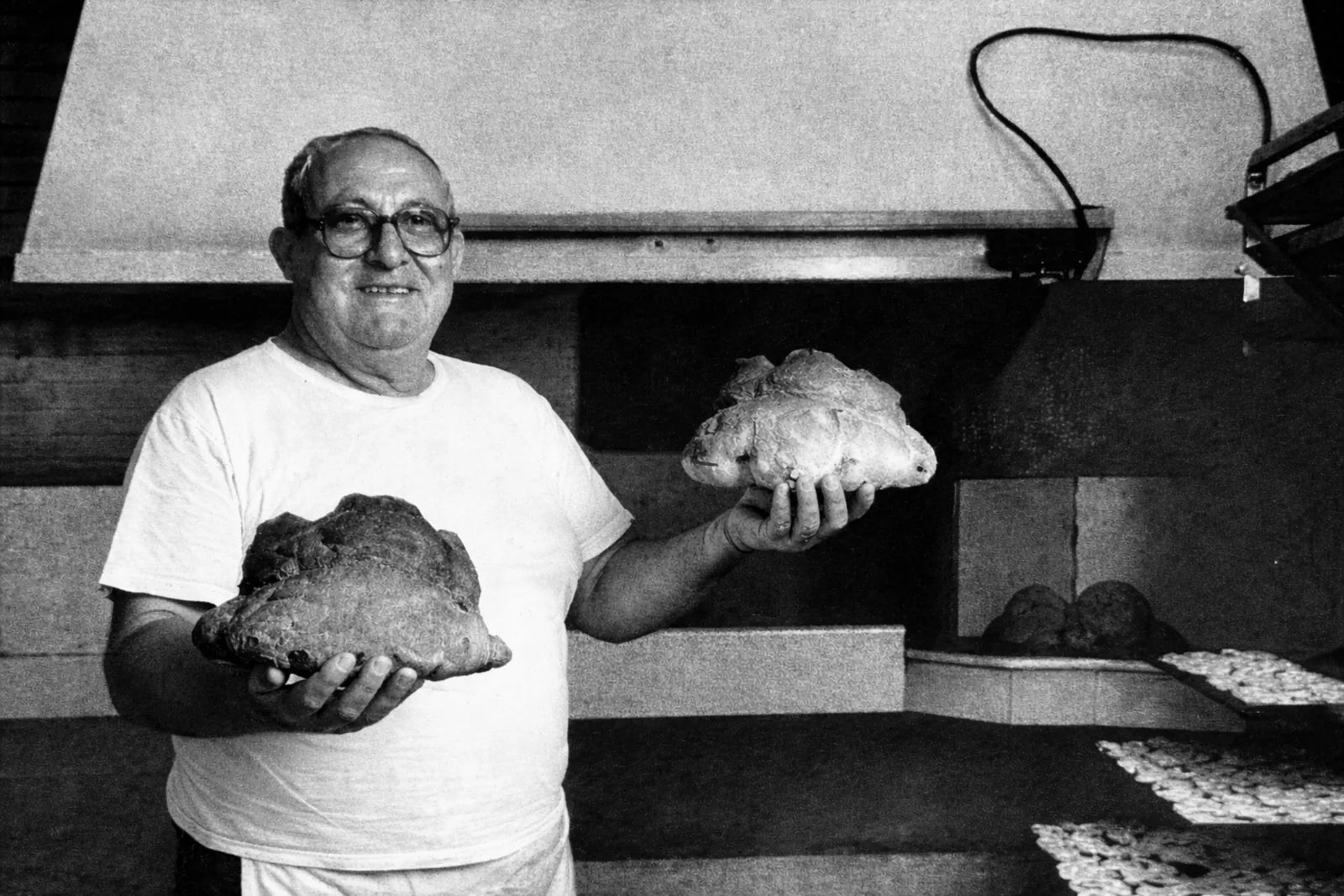 Santino Perrone mostra due pani artigianali di Matera davanti al forno in una foto storica in bianco e nero.
